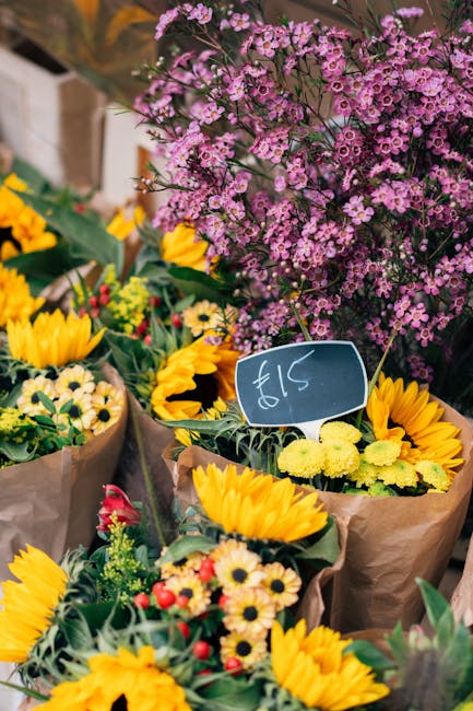 A vibrant array of fresh floral arrangements displayed at a flower market, featuring bright yellow sunflowers with large, dark centers, small white daisies with yellow centers, and clusters of pink an
