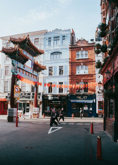 The image depicts a vibrant street scene in Chinatown London, featuring traditional Chinese architectural elements such as a decorative gate with ornate, curved eaves and intricate dragon motifs, pain